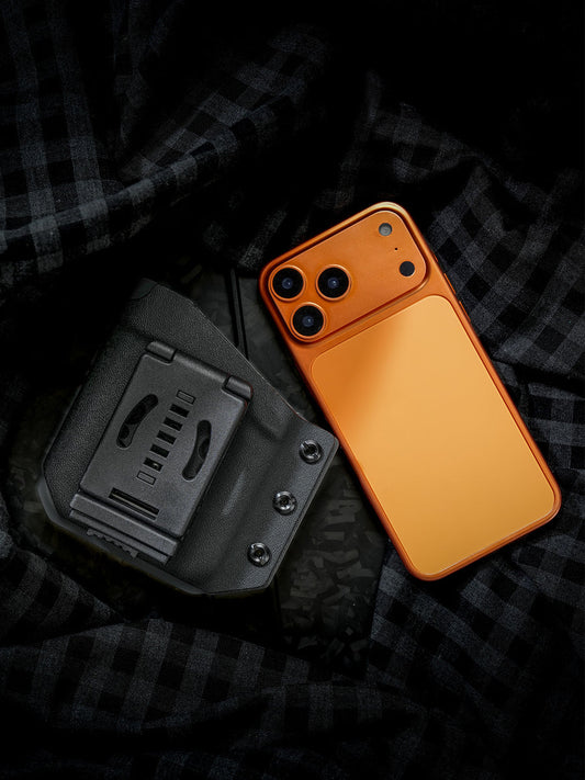 Rear view of the Black-Grey phone case for iPhone 17 Pro and iPhone 17 Pro Max, showing the integrated black belt clip beside an orange smartphone.