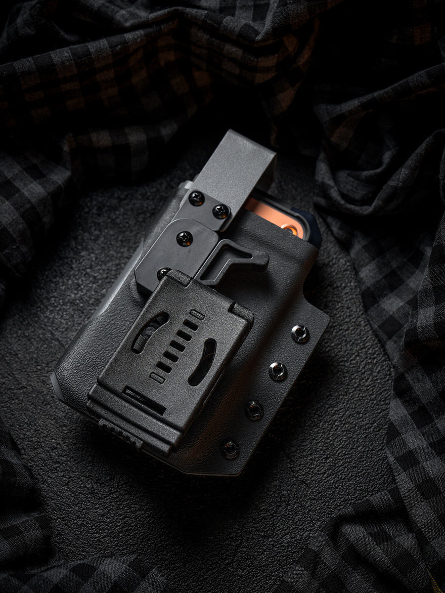 Rear view of the black Single Skeleton Window phone case with belt clip, shown with a smartphone inside on a dark plaid fabric background.