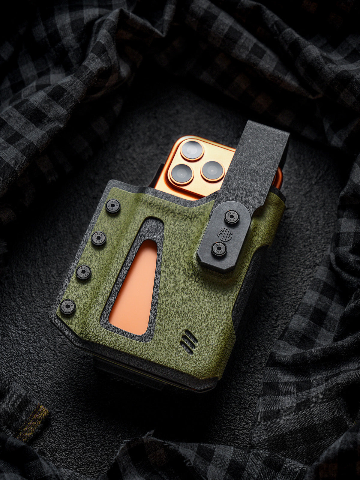 Front view of the olive green Single Skeleton Window phone case with a smartphone inserted, displayed on a dark plaid fabric background.