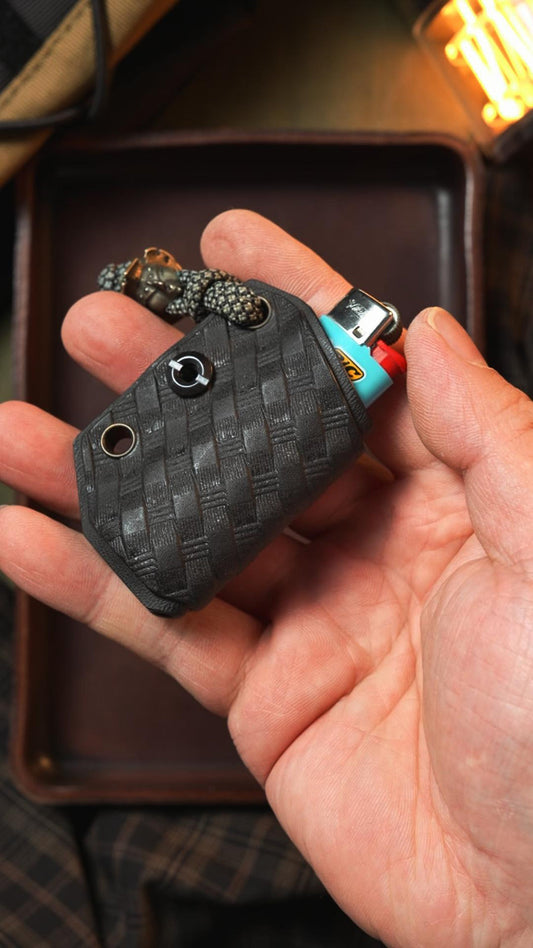 TACTICALGEEK Woven Black Kydex sheath for BIC lighter with textured pattern and lanyard attachment, shown handheld.