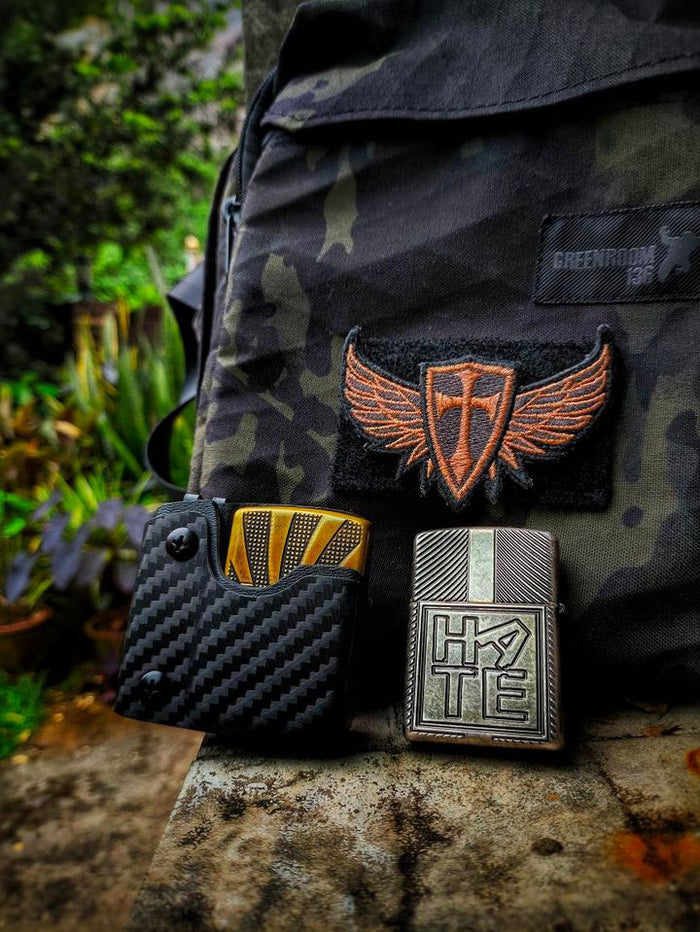 Outdoor lifestyle image of the carbon fiber TX2 KYDEX EDC Zippo lighter sheath displayed next to a Zippo lighter and backpack.
