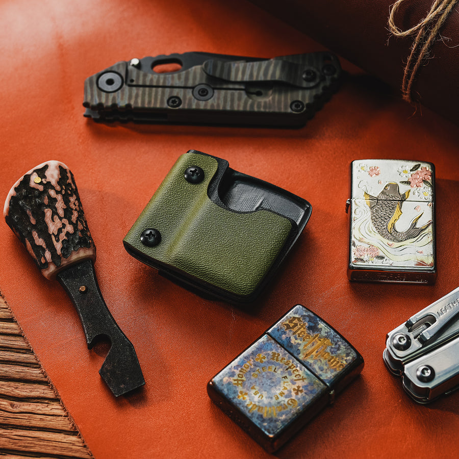 Desktop lifestyle image of the green TX2 KYDEX EDC Zippo lighter sheath displayed with EDC gear and lighters.