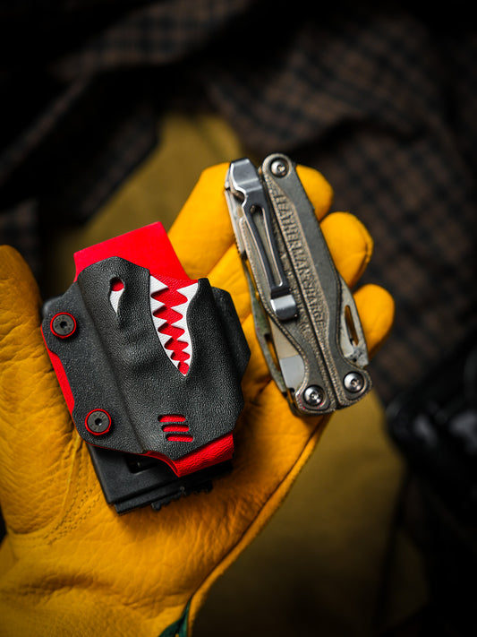 Shark-style TX15 multi-tool sheath for Leatherman Charge with belt clip, shown in a gloved hand beside the multi-tool.