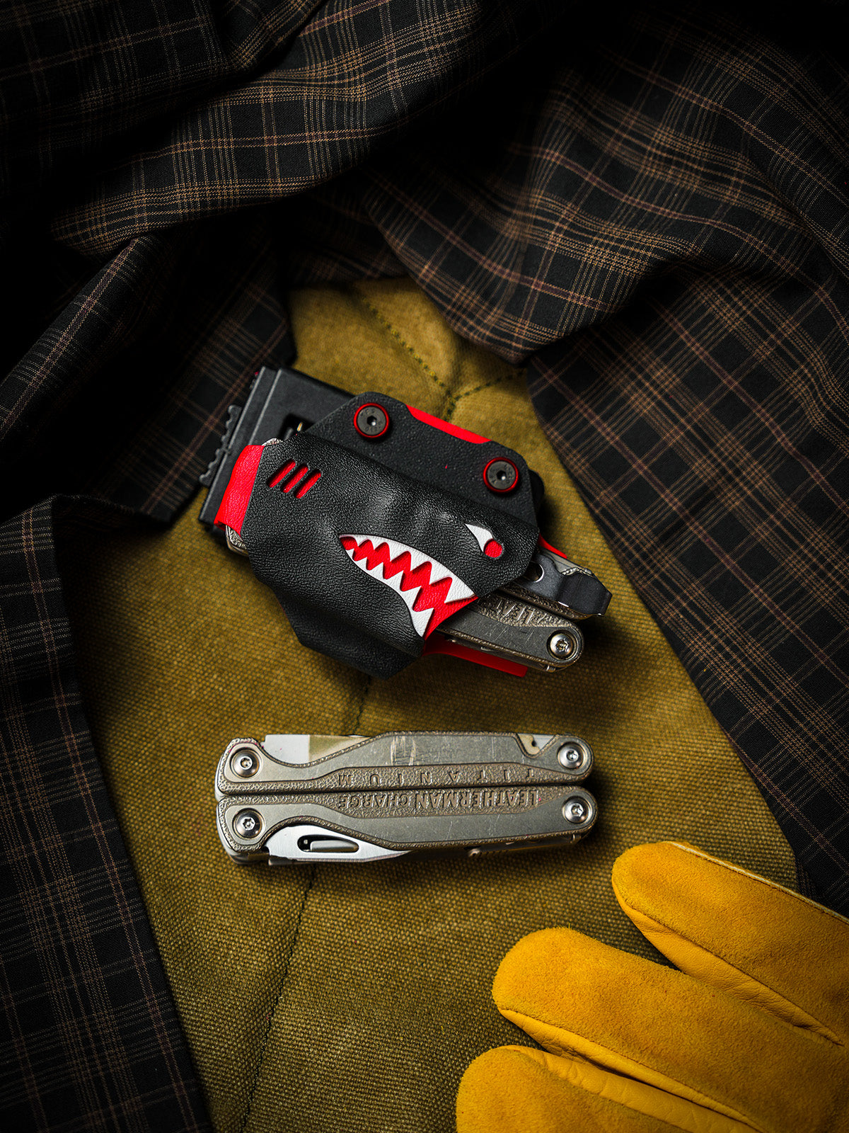 Shark-style TX15 multi-tool sheath for Leatherman Charge with belt clip, displayed with the tool on a fabric surface.