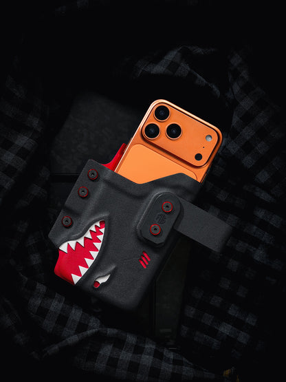Close product view of the black and red TACTICALGEEK TG EDC KYDEX shark phone sheath holding an orange iPhone 17 Pro Max.