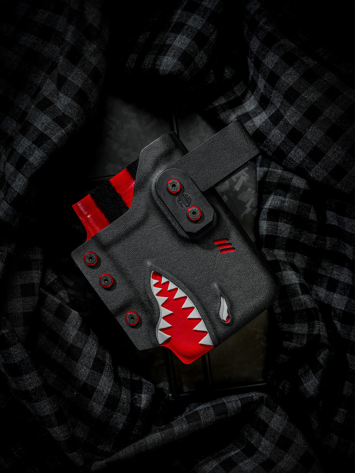 Black and red shark-style TACTICALGEEK TG EDC KYDEX phone sheath for iPhone 17 Pro and iPhone 17 Pro Max, front product view on dark plaid fabric.