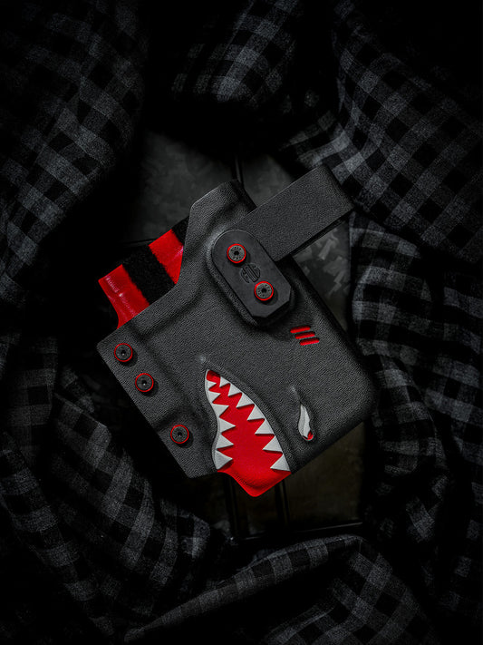Black and red shark-style TACTICALGEEK TG EDC KYDEX phone sheath for iPhone 17 Pro and iPhone 17 Pro Max, front product view on dark plaid fabric.