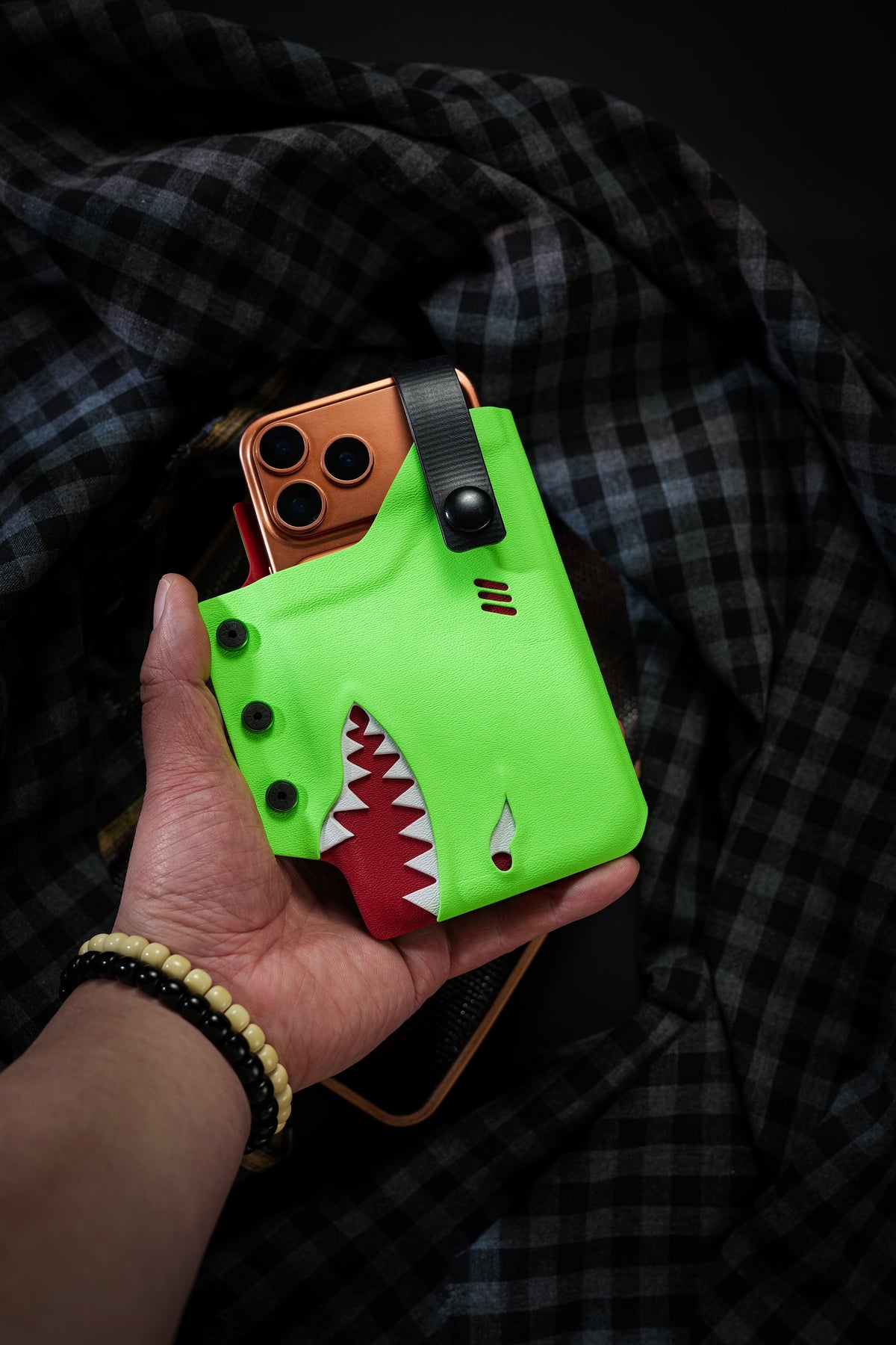 Product display of the neon green TACTICALGEEK TG EDC KYDEX shark phone sheath for iPhone 17 Pro and iPhone 17 Pro Max on a dark tray.