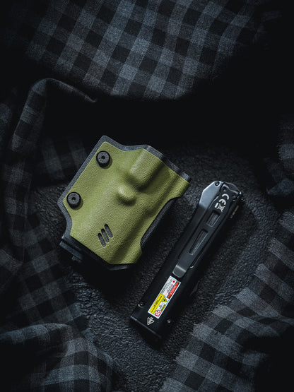 Flat lay of the olive green TX17 flashlight sheath for Nitecore EDC17 placed beside the flashlight on a dark plaid fabric background.