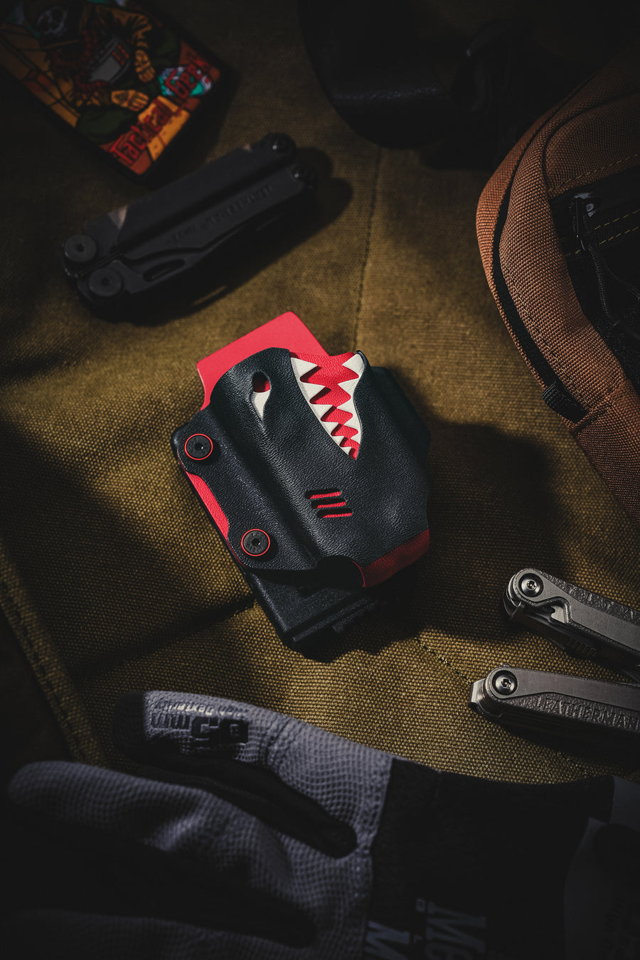 Front view of the TX19 multi-tool sheath for Leatherman Surge placed on fabric, showing the shark-inspired black and red design.
