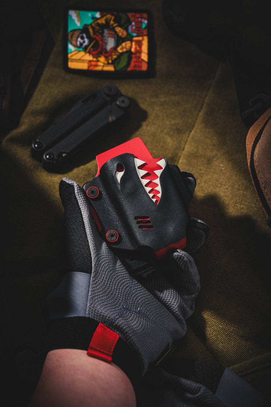 Hand holding the TX19 shark-style multi-tool sheath for Leatherman Surge, shown in black and red with a rugged EDC background.