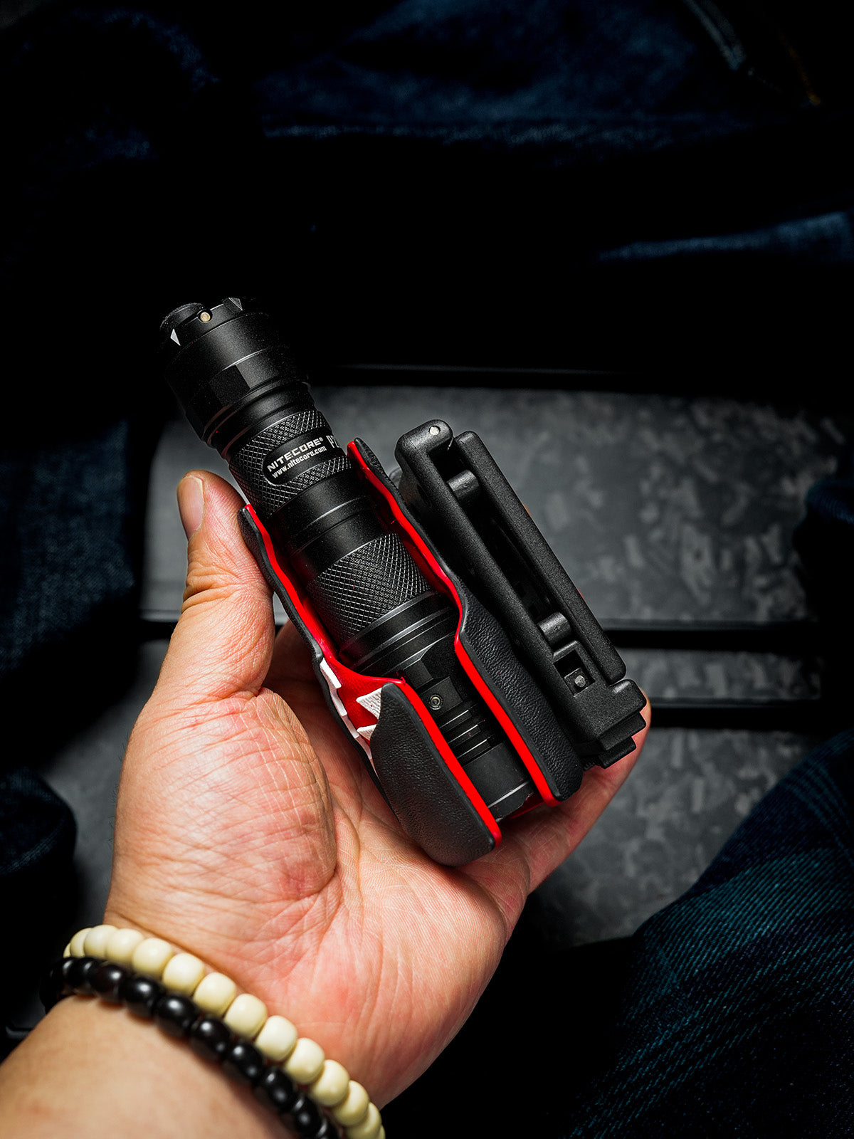 Hand holding the TX22 flashlight sheath for Nitecore P20ix from the side, showing the inserted flashlight, red inner lining, and attached belt clip.