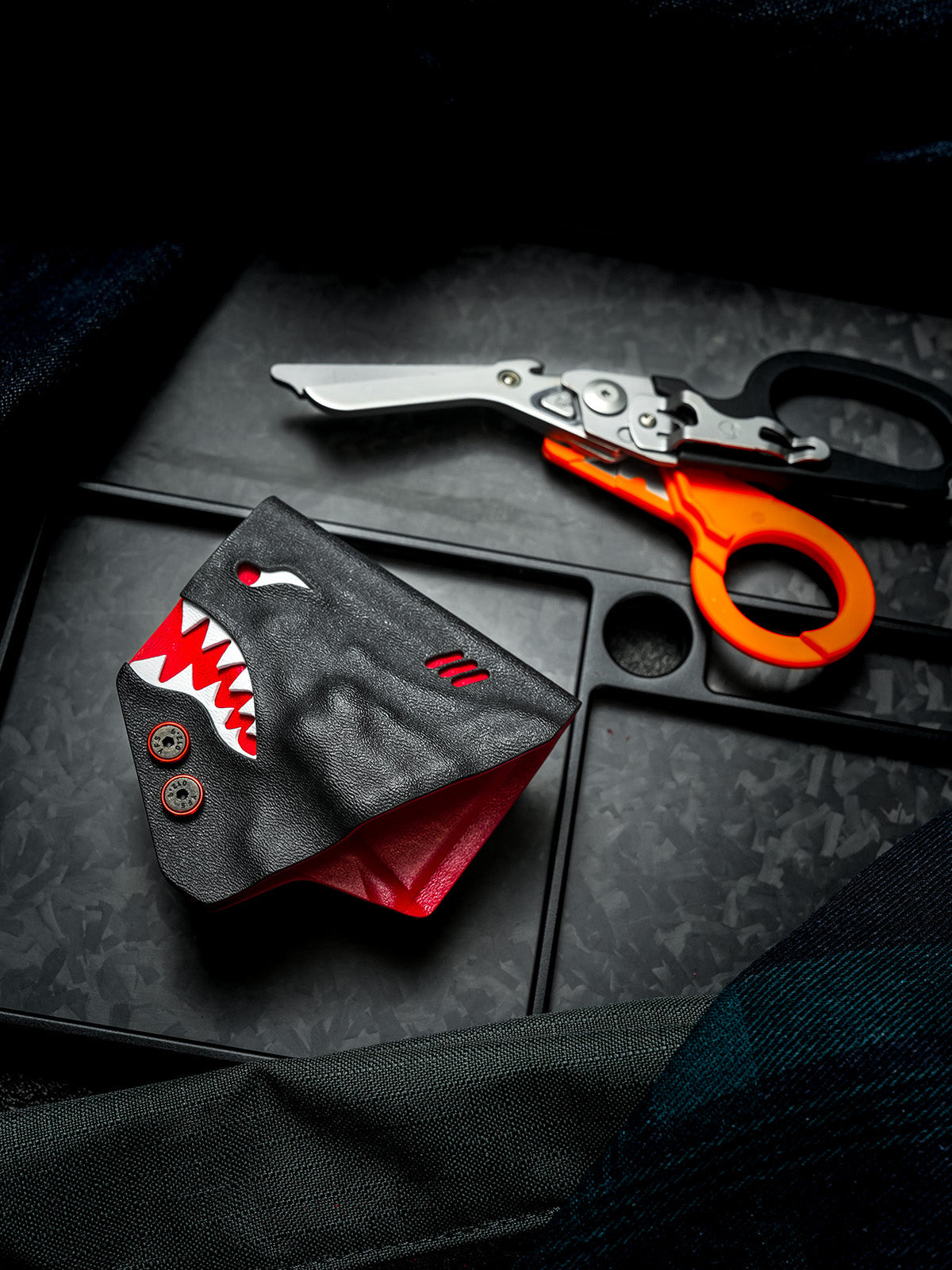 Front view of the shark-style TX24 sheath for Leatherman Raptor, with rescue shears placed in the background on a dark surface.