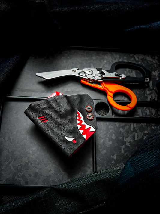 Shark-shaped TX24 multi-tool sheath for Leatherman Raptor displayed beside unfolded rescue shears on a dark tabletop.