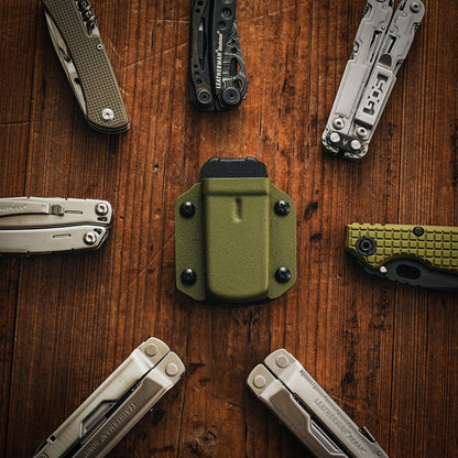 Flat lay image of the olive green TX3 Multitool Sheath centered on a wooden surface surrounded by multitools and folding knives.